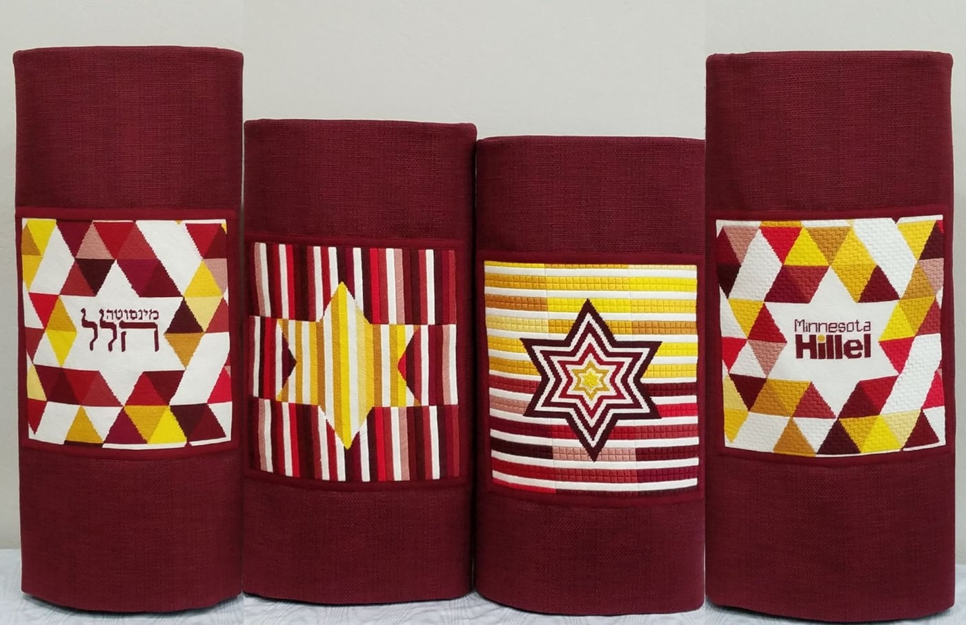 A set of burgundy needlepoint torah covers, with geometric decorations